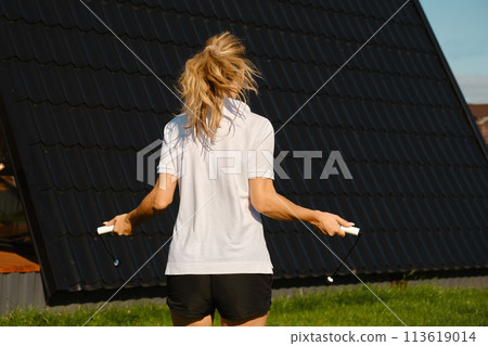 woman jumps with a rope on the lawn in front of the house 113619014