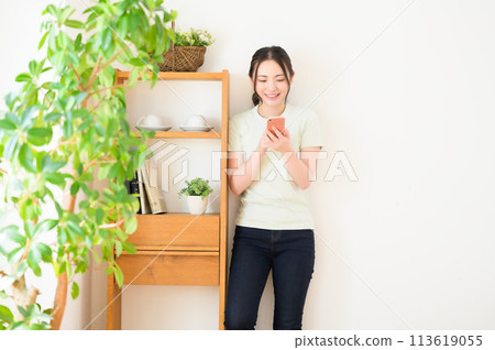 A young woman standing by a wall and looking at her smartphone A young woman standing by a wall and looking at her smartphone 113619055