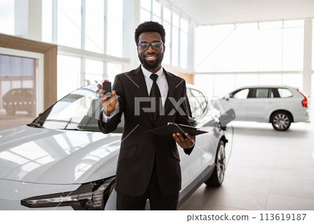 African salesman giving to customer key at new car in showroom. 113619187