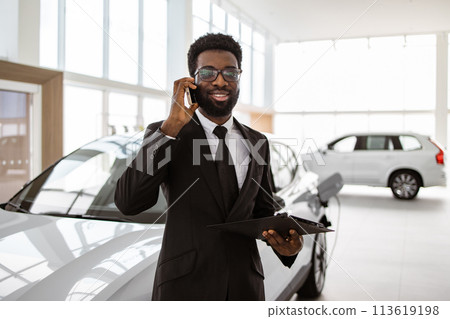 Car dealer holding clipboard in automobile showroom. 113619198