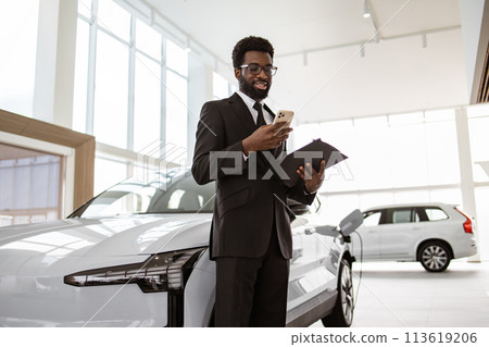 Smiling salesman using smartphone while having business call at car showroom. Smiling salesman using smartphone while having business call at car showroom. 113619206