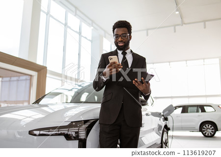 Smiling salesman using smartphone while having business call at car showroom. Smiling salesman using smartphone while having business call at car showroom. 113619207