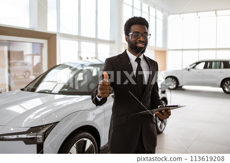 Young successful manager on background of rows of new car dealership crossovers. 113619208