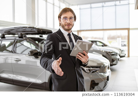 Bearded manager shaking hand with buyer on background of rows of crossovers. 113619304