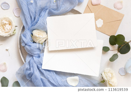 Cards near light blue tulle fabric knot and cream roses on plates top view copy space, wedding mockup 113619539