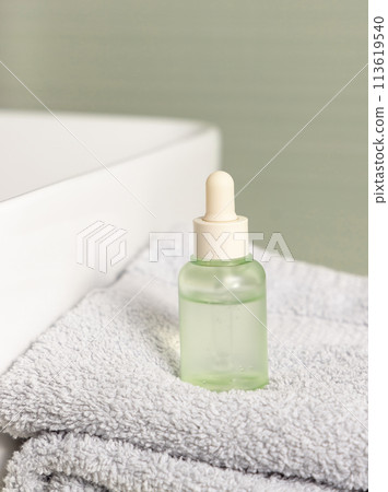 Green dropper bottle near basin on light grey towel against green wall in bath, mockup Green dropper bottle near basin on light grey towel against green wall in bath, mockup 113619540