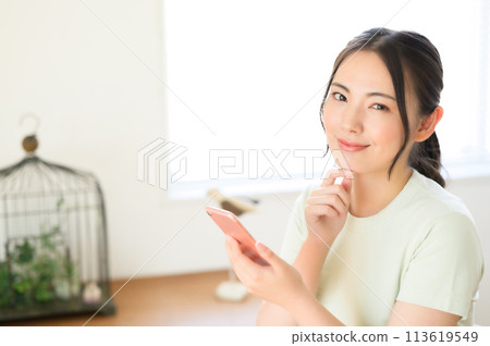 A woman sitting on a chair and looking at her smartphone A woman sitting on a chair and looking at her smartphone 113619549