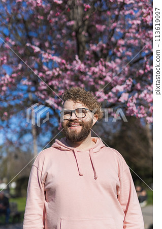 Man allergic enjoying after treatment from seasonal allergy at spring. Portrait of happy bearded man smiling in front of blossom tree at springtime. Spring blooming and allergy concept. Copy space 113619997