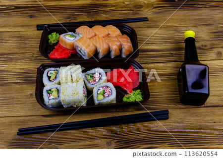 Set of sushi rolls in plastic boxes, soy sauce and chopsticks on wooden table. Sushi for take away or delivery of sushi in plastic containers 113620554
