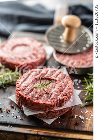 Fresh raw ground beef patties with rosemary salt and pepper made in a meat form on a cutting board 113620735