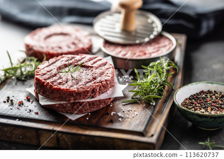 Fresh raw ground beef patties with rosemary salt and pepper made in a meat form on a cutting board Fresh raw ground beef patties with rosemary salt and pepper made in a meat form on a cutting board 113620737