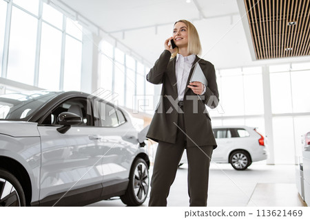 Smiling saleswoman smartphone while having business call at car showroom. 113621469