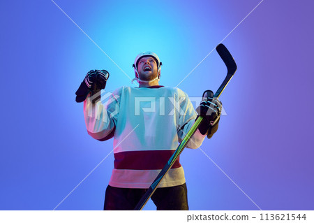 Man, hockey player in helmet, uniform and stick expressing emotions of win against gradient blue background in neon light Man, hockey player in helmet, uniform and stick expressing emotions of win against gradient blue background in neon light 113621544