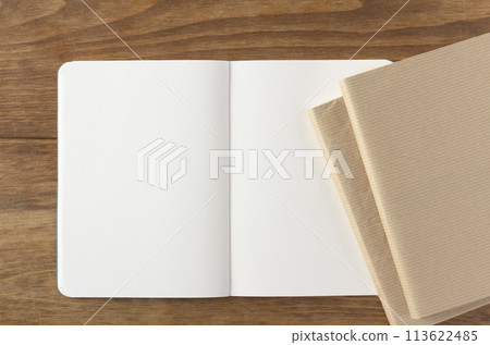 A blank notebook and two books placed on a wooden desk A blank notebook and two books placed on a wooden desk 113622485