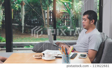 A man in casual wear using laptop while he is working at home office. A man in casual wear using laptop while he is working at home office. 113622681