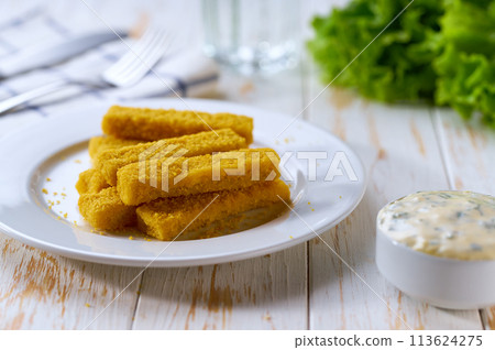 Tasty crispy deep fried fish fingers served with lemon and tartar sauce on wooden table. 113624275