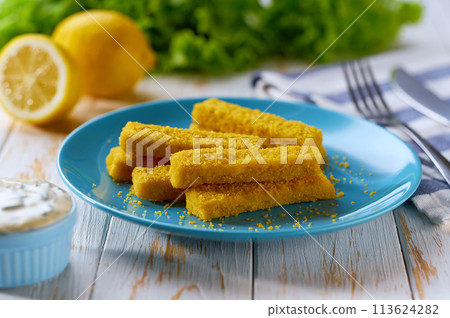 Tasty crispy deep fried fish fingers served with lemon and tartar sauce on wooden table. 113624282