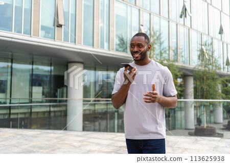 African american man talking on smartphone on street in city outdoor. Man with cell phone chatting with friends. Smiling person making answering call by cellphone. Guy having conversation by mobile 113625938