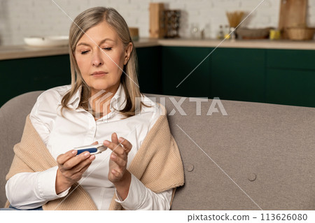 Good-looking mid aged woman sitting on the sofa and making blood sugar test 113626080