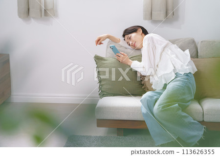 Middle-aged woman relaxing while looking at her smartphone Middle-aged woman relaxing while looking at her smartphone 113626355