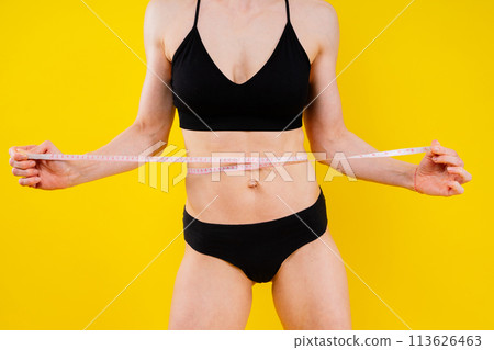 Athletic slim woman measuring her waist by measure tape after a diet over dark yellow background Athletic slim woman measuring her waist by measure tape after a diet over dark yellow background 113626463