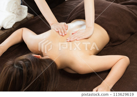 A woman is getting an oil massage on her back. 113629619