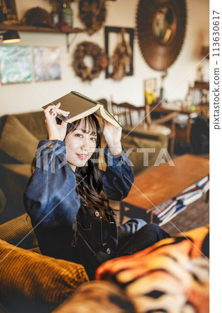 一位女士在時尚的古董咖啡館裡頭頂一本書放鬆身心 一位女士在時尚的古董咖啡館裡頭頂一本書放鬆身心 113630617