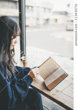 度假時，年輕女子在咖啡館靠窗的座位上喝咖啡時讀書 113630732