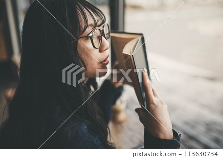 A young woman reading a book on her day off while drinking coffee at a window seat in a cafe 113630734