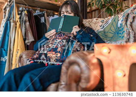 度假時，年輕女子在咖啡館靠窗的座位上喝咖啡時讀書 113630748