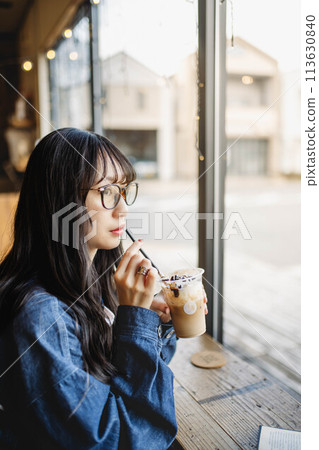 Young long-haired woman drinking a drink at a window seat in a cafe Young long-haired woman drinking a drink at a window seat in a cafe 113630840