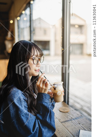 Young long-haired woman drinking a drink at a window seat in a cafe Young long-haired woman drinking a drink at a window seat in a cafe 113630841