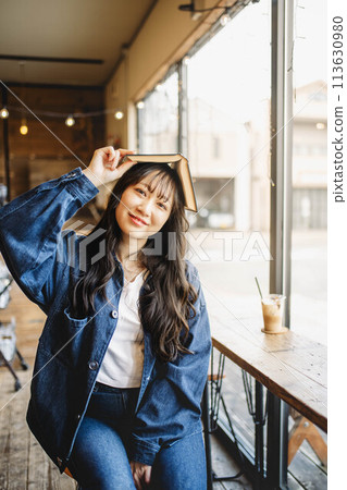 一位年輕女子在一家古董咖啡館的靠窗座位上頭頂一本書休息 113630980