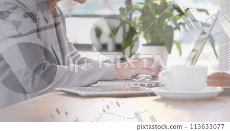 Digital composite of two guys facing each other while working on a laptop at a desk with graphs and Digital composite of two guys facing each other while working on a laptop at a desk with graphs and 113633077