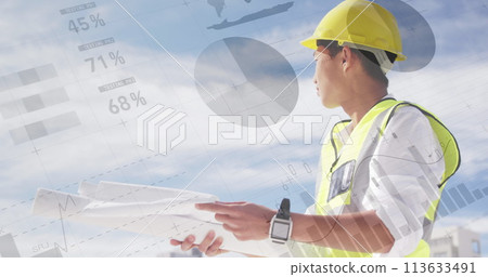 Asian male architect with plans atop a building, graphs in front 113633491