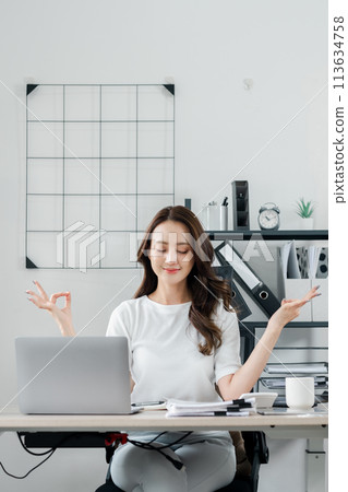 Businesswoman closes her eyes and meditates, practicing mindfulness to maintain balance during a busy workday. 113634758