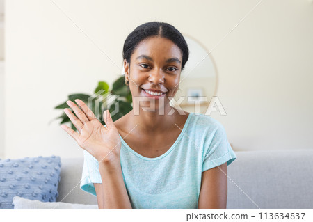 Young biracial woman waves cheerfully from her home on a video call Young biracial woman waves cheerfully from her home on a video call 113634837