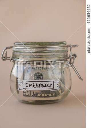 Saving Money In Glass Jar filled with Dollars banknotes. EMERGENCY transcription in front of jar. Managing personal finances extra income for future insecurity 113634882