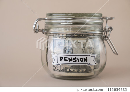 Glass jar full of American currency dollars cash banknote with text PENSION. Preparation saving money. Moderate consumption and economy Glass jar full of American currency dollars cash banknote with text PENSION. Preparation saving money. Moderate consumption and economy 113634883