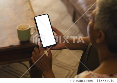 A mature biracial woman checks her smartphone at home, with copy space unaltered A mature biracial woman checks her smartphone at home, with copy space unaltered 113634919