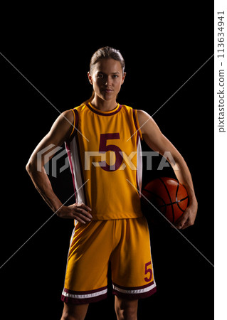 Confident female basketball player poses with a ball on a black background Confident female basketball player poses with a ball on a black background 113634941