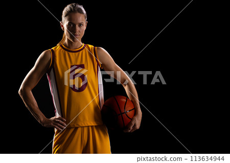 Confident young Caucasian female basketball player poses in basketball attire, with copy space on bl 113634944