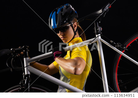 Young Caucasian female cyclist prepares her bicycle for a night ride, with copy space 113634951
