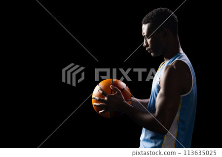 African American athlete holding a basketball on a black background, with copy space 113635025