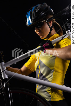 Cyclist in yellow jersey carries her bike, with copy space 113635063
