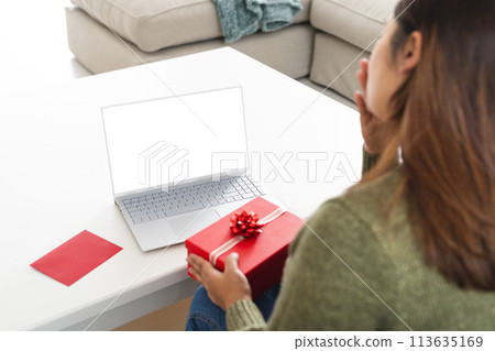 Young biracial woman at home with a gift on a video call, with copy space 113635169