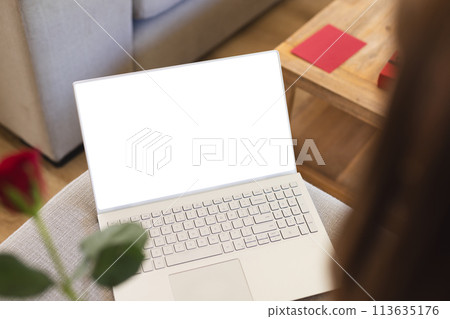 A laptop with a white screen is open on a wooden table, with copy space 113635176