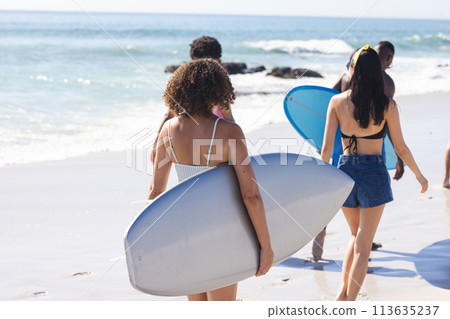 Young women carry surfboards on a sunny beach Young women carry surfboards on a sunny beach 113635237