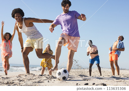 Diverse friends enjoy a lively game of soccer on the beach Diverse friends enjoy a lively game of soccer on the beach 113635306