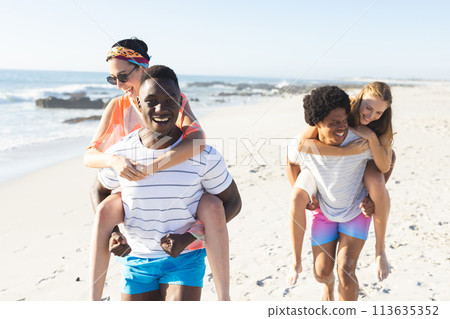 Diverse couples enjoy a piggyback ride on the beach 113635352